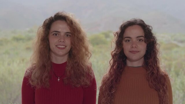 Hermanas gemelas de frente mirando a cámara en un día nublado con las montañas de fondo