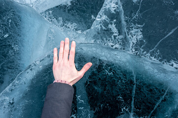 Woman's hand touches the clear blue cracked ice of Lake Baikal. Top view