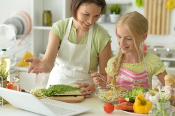 girl with her mother cooking and looking at laptop