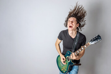 Young man is playing an electric guitar singing and waving his long hair. Emotional performance of rock and roll - 420746327