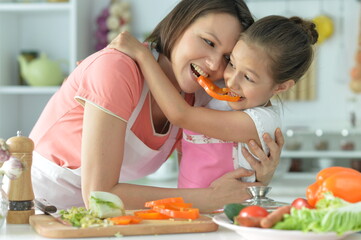 Cute little girl with her mother cooking together at kitchen table