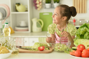 Cute girl preparing delicious fresh salad in kitchen
