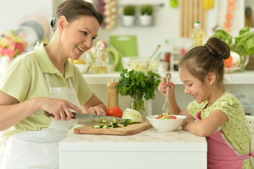 Cute little girl with her mother cooking together at kitchen table