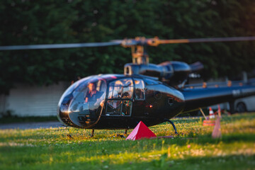 Civil black helicopter getting ready to fly, commercial charter private copter at helipad airfield with people embarking, pilot, getting a pilot course license concept, chopper landing on green grass © tsuguliev