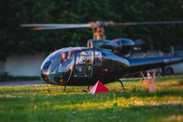 Civil black helicopter getting ready to fly, commercial charter private copter at helipad airfield with people embarking, pilot, getting a pilot course license concept, chopper landing on green grass