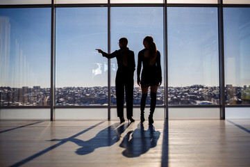 Two business women enjoying the city view and talking while standing by the large window in the office