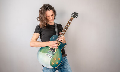 Young man is playing solo an electric guitar and waving his long hair. Emotional performance of...