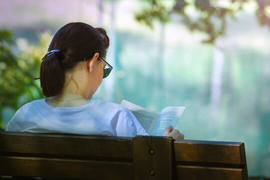 young woman sitting on a bench reading a book, she's wearing asual Clothing and sunglasses