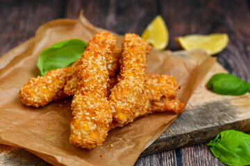 
 Crispy  deep fried home made    chicken strips with sesame seeds.Chicken  breast fillets  with  lemons  and fresh   basil on wooden rustic background. Ketogenic diet food