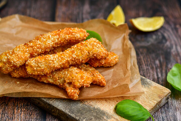 
 Crispy  deep fried home made    chicken strips with sesame seeds.Chicken  breast fillets  with  lemons  and fresh   basil on wooden rustic background. Ketogenic diet food