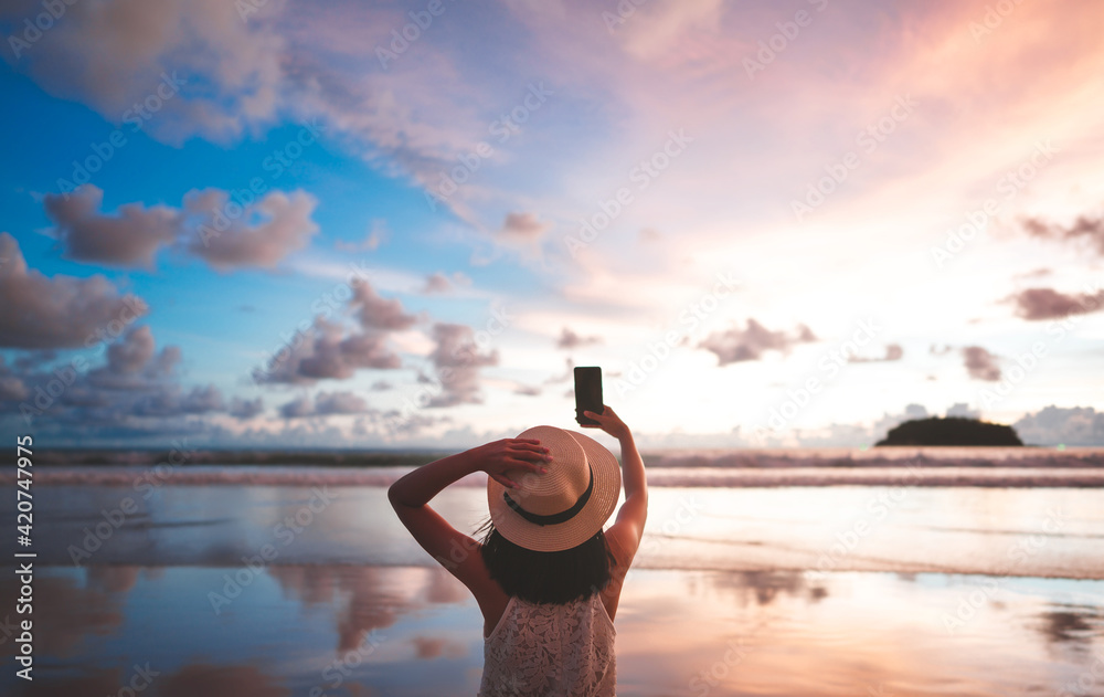 Wall mural rear view of adult woman relax in nature travel on beach sea using smart phone with sunset sky.