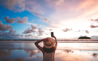 Rear view of adult woman relax in nature travel on beach sea using smart phone with sunset sky. - obrazy, fototapety, plakaty