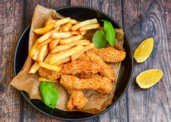 
 Crispy  deep fried   chicken strips  with sesame seeds and french fries . Breaded  with cornflakes chicken  breast fillets  with chilly peppers and fresh   basil on wooden rustic background