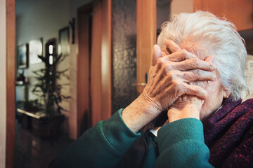 Desolate old woman at home. She's covers her face