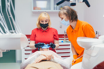 Senior experienced female dentist fills the canal with modern equipment in a dental clinic. Sealing of channels. New methods treatment tools teeth with a special photopolymer substance
