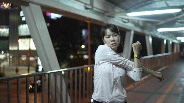 Female marathon athletes, asia, warm-up, arms stretching, running workout at night on the urban environment