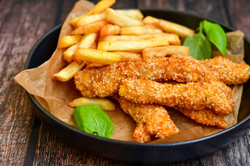 
 Crispy  deep fried   chicken strips  with sesame seeds and french fries . Breaded  with cornflakes chicken  breast fillets  with chilly peppers and fresh   basil on wooden rustic background
