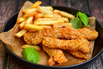 
 Crispy  deep fried   chicken strips  with sesame seeds and french fries . Breaded  with cornflakes chicken  breast fillets  with chilly peppers and fresh   basil on wooden rustic background
