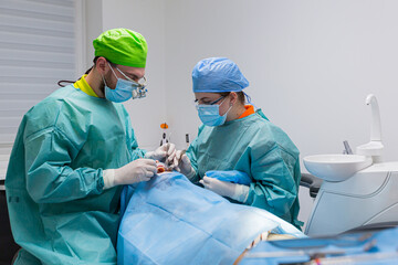 Team of dental surgeons performs surgery on teeth. in a modern clinic. Young dentist. Teamwork. Tooth doctor orthodontist surgeon doing medical operation on root canals. Stomatology office. 