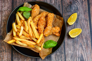 
 Crispy  deep fried   chicken strips  with sesame seeds and french fries . Breaded  with cornflakes chicken  breast fillets  with chilly peppers and fresh   basil on wooden rustic background