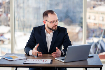Fototapeta na wymiar Adult male mentor, director, businessman in glasses and a suit studying documents while sitting at the table. Working day concept
