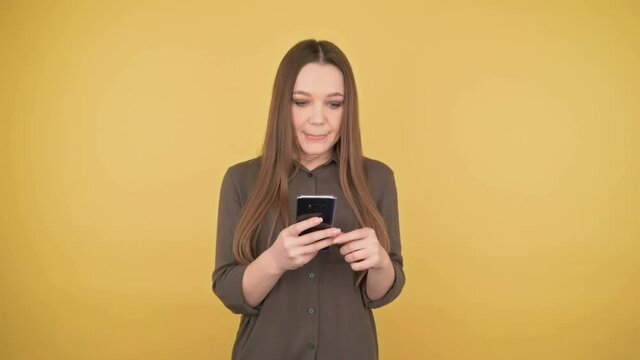 I won. Shocked joyful business woman crosser fingers on a swell on an isolated yellow background with looking looks at the smartphone
