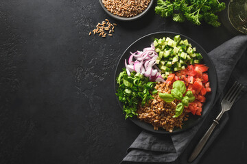 Cooked Whole Grain cereal spelt salad with seasonal vegetables in bowl on black background.
