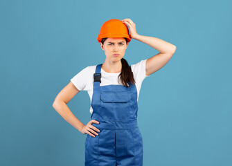 Thoughtful handywoman in protective helmet and coveralls touching head in confusion