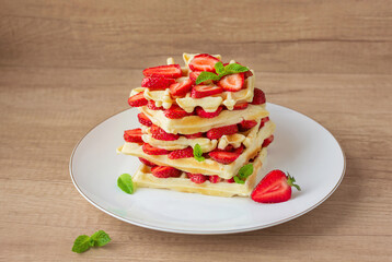 Belgian waffles with fresh strawberry and mint on white plate. Wooden background