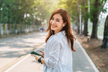 Portrait of happy asian woman using the small talk headphones to make a happy phone call in the street in a sunny summer day.