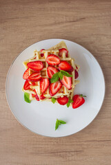 Belgian waffles with fresh strawberry and mint on white plate. Top view