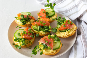 Delicious hearty appetizer, salmon toast on a white plate, round fried bun with red fish, cucumber, hollandaise sauce and pea sprouts