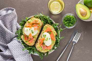 Delicious hearty breakfast, sandwiches with avocado paste, salmon and mozzarella on a plate with arugula and pea sprouts