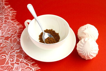 One white cup of coffee, teaspoon, marshmallows and lace tablecloth on a red table.