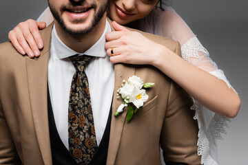 Cropped view of smiling bride embracing happy Arabian fiancé isolated on grey