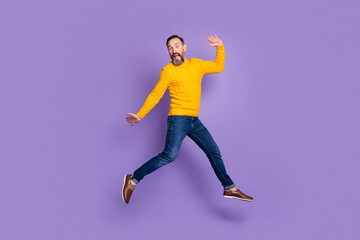 Fototapeta na wymiar Photo of excited man jump run raise hands wear yellow pullover jeans footwear isolated violet background