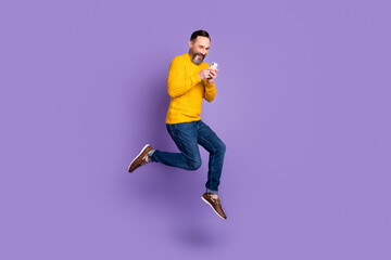 Photo of funny man jump run hold telephone look screen wear yellow pullover jeans shoes isolated purple background