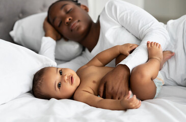 Cute little African American baby sleeping in bed with mom