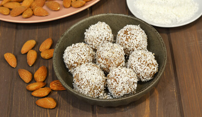 Marzipan candy being covered with grated coconut on wooden background. Round white candy with coconut flakes. Homemade snacks. Healthy food for weekdays and holidays