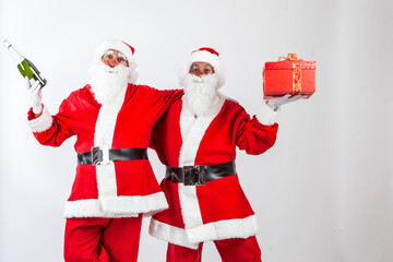 coppia di babbi natale gioca e scherza con in mano  un regalo color rosso e una bottiglia di spumante , isolati su sfondo bianco