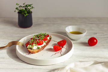 Tasty sandwich with cherry tomatoes, micro greens and soft cheese on wholegrain bread on light wooden background. Healthy breakfast or lunch concept.