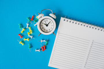 planner, thumbtacks and white alarm clock on grunge blue background