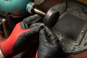 man wearing protective gloves polishes a silver ring with a grinder