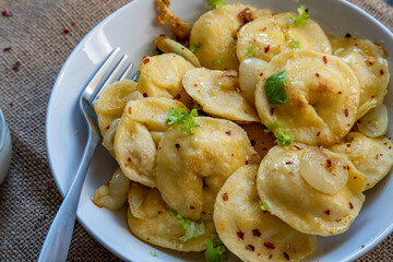 Pelmeni dumplings making process: Cooked pelmeni filled with meat in a bowl with seasoning and onions on rustic cloth. Gluten free recipe for traditional Russian cuisine. handmade ravioli or dumplings
