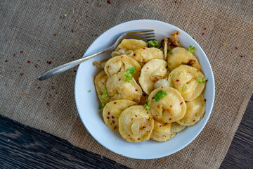 Pelmeni dumplings making process: Cooked pelmeni filled with meat in a bowl with seasoning and onions on rustic cloth. Gluten free recipe for traditional Russian cuisine. handmade ravioli or dumplings
