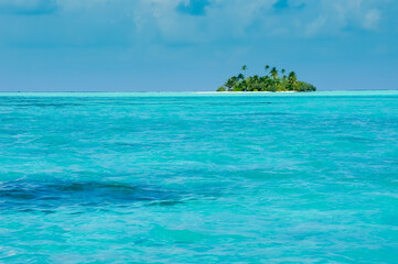 Uninhabited tropical island with palm trees. Cloudy sky and turquoise lagoon