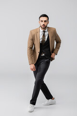 full length view of young muslim man in trendy suit  and sneakers looking at camera on grey