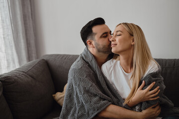 Young couple sitting at a sofa with a warm blanket. Man kissing a woman. Romantic relationship