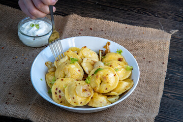 Pelmeni dumplings making process: Hand eating cooked pelmeni stuffed with meat in a bowl with seasoning, onions and sour cream using a fork. Gluten free recipe for traditional Russian cuisine. Rustic.