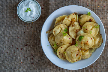 Pelmeni dumplings making process: Cooked pelmeni stuffed with meat in a bowl with seasoning, onions and sour cream. Gluten free recipe for traditional Russian cuisine. handmade ravioli or dumplings.